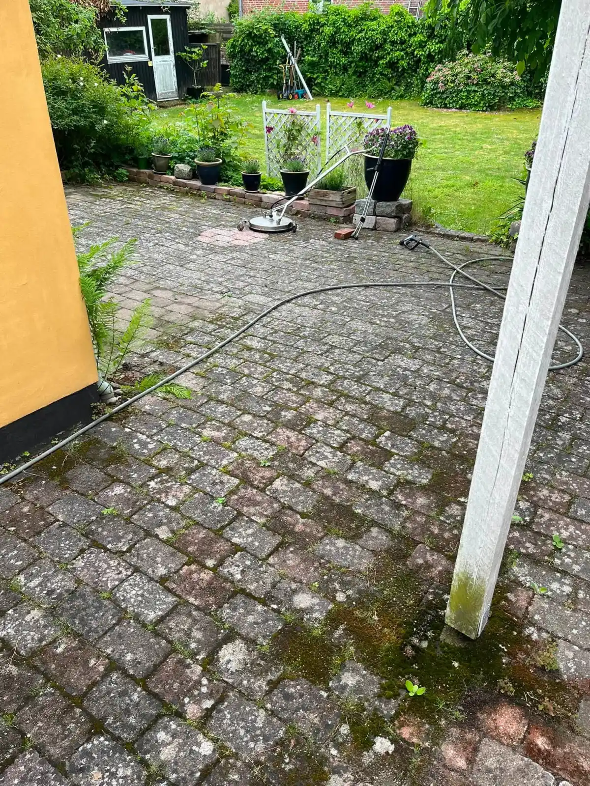 Rød og grå belægning ved gul mur før fliserens